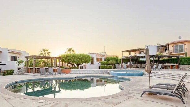 A pool area with lounge chairs and umbrellas, surrounded by buildings and greenery. - Casas TZL (Cabo San Lucas)
