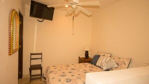 A bedroom with a bed, a chair, a nightstand with a lamp, a ceiling fan, and a TV mounted on the wall. - Casas TZL (Cabo San Lucas)