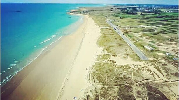 Vista aérea de una zona costera con playa, carretera y edificios dispersos.