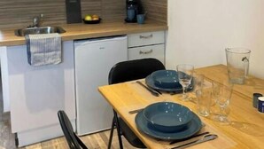 Cocina compacta con armarios blancos, encimera de madera, pileta y cafetera. Hay una mesa de comedor con platos azules, vasos y cubiertos.