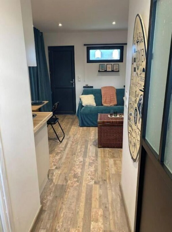 A narrow hallway leading to a bedroom with a bed, a television, and a wall clock.