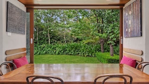 A dining area with a wooden table and chairs, a bench, and a view of a lush garden through an open door. - Summer House - 2 Bedroom House (Wentworth Falls)
