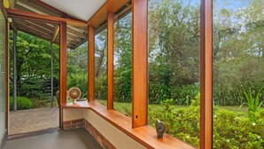 A modern interior with large windows, wooden beams, and a view of a lush garden. - Summer House - 2 Bedroom House (Wentworth Falls)