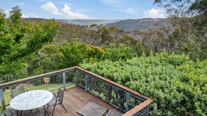 A deck with a table and chairs overlooking a mountainous landscape. - Summer House - 2 Bedroom House (Wentworth Falls)