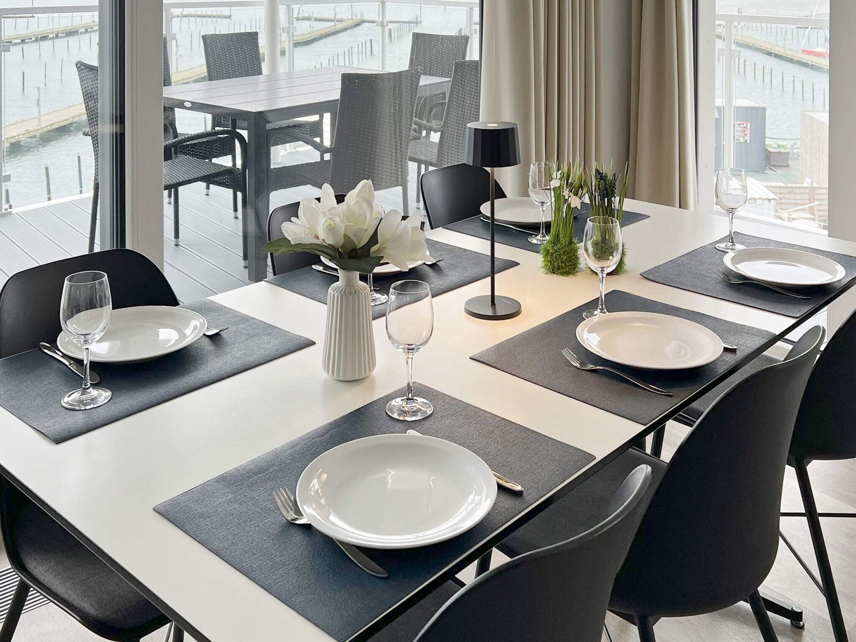 A dining table set with plates, glasses, and a vase of flowers, with chairs around it.