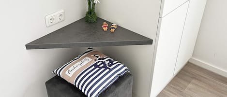 A corner of a room with a grey shelf, a small plant, and a cushion with a striped pattern.