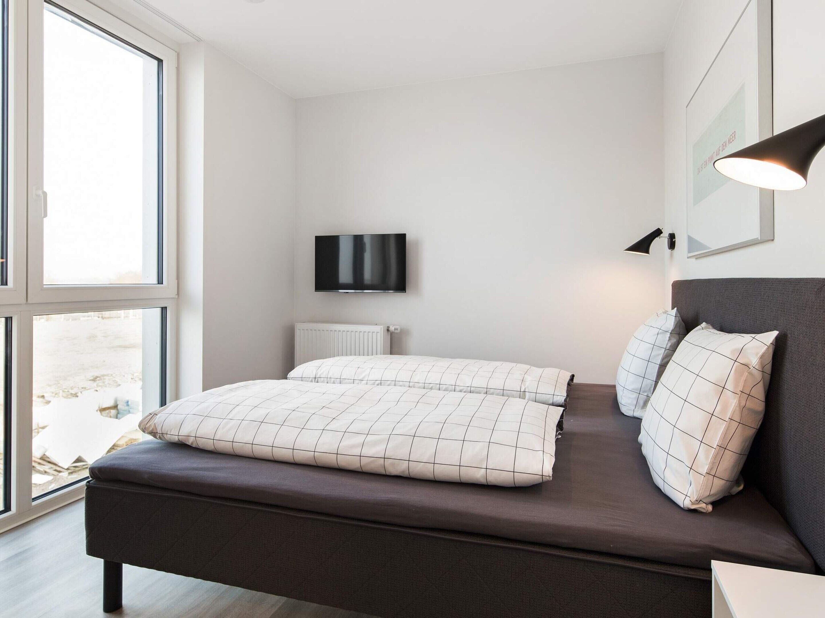 A modern bedroom with a bed, a flat-screen TV, and a window.