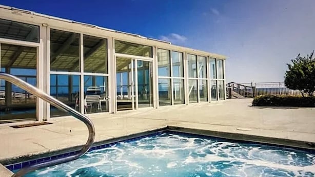 A swimming pool with a glass enclosure and a metal staircase leading to a building with large windows. - GulfSide Oasis-On The Beach (Pensacola)