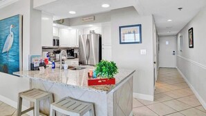 A modern kitchen with a marble island, stainless steel appliances, and a view into the living area. - GulfSide Oasis-On The Beach (Pensacola)
