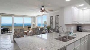 A kitchen with a large island, white cabinets, and a view of the ocean. - GulfSide Oasis-On The Beach (Pensacola)