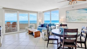 A spacious living area with a balcony, a ceiling fan, and a dining table with chairs. - GulfSide Oasis-On The Beach (Pensacola)