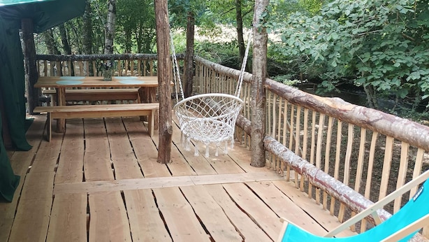 Een houten terras met picknicktafels en een witte stoel, omringd door een houten hek en bomen.