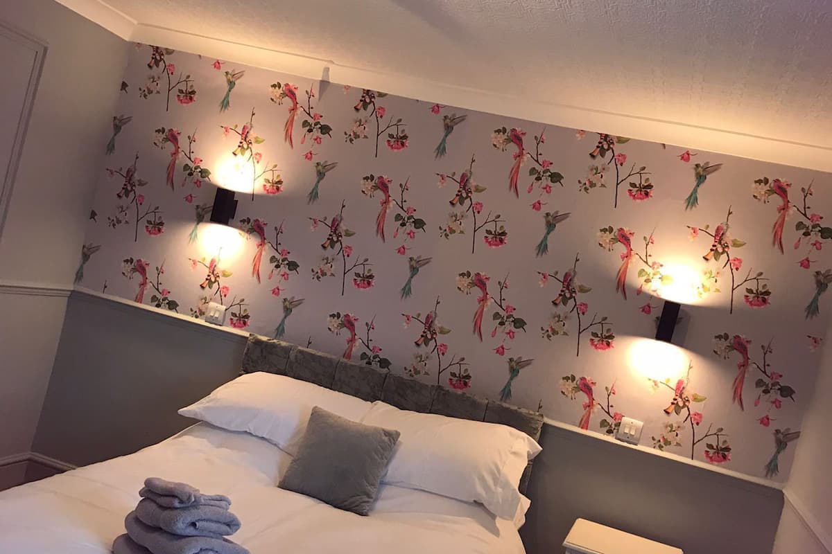A bedroom with a bed, two bedside lamps, a nightstand, and a floral-patterned wall.
