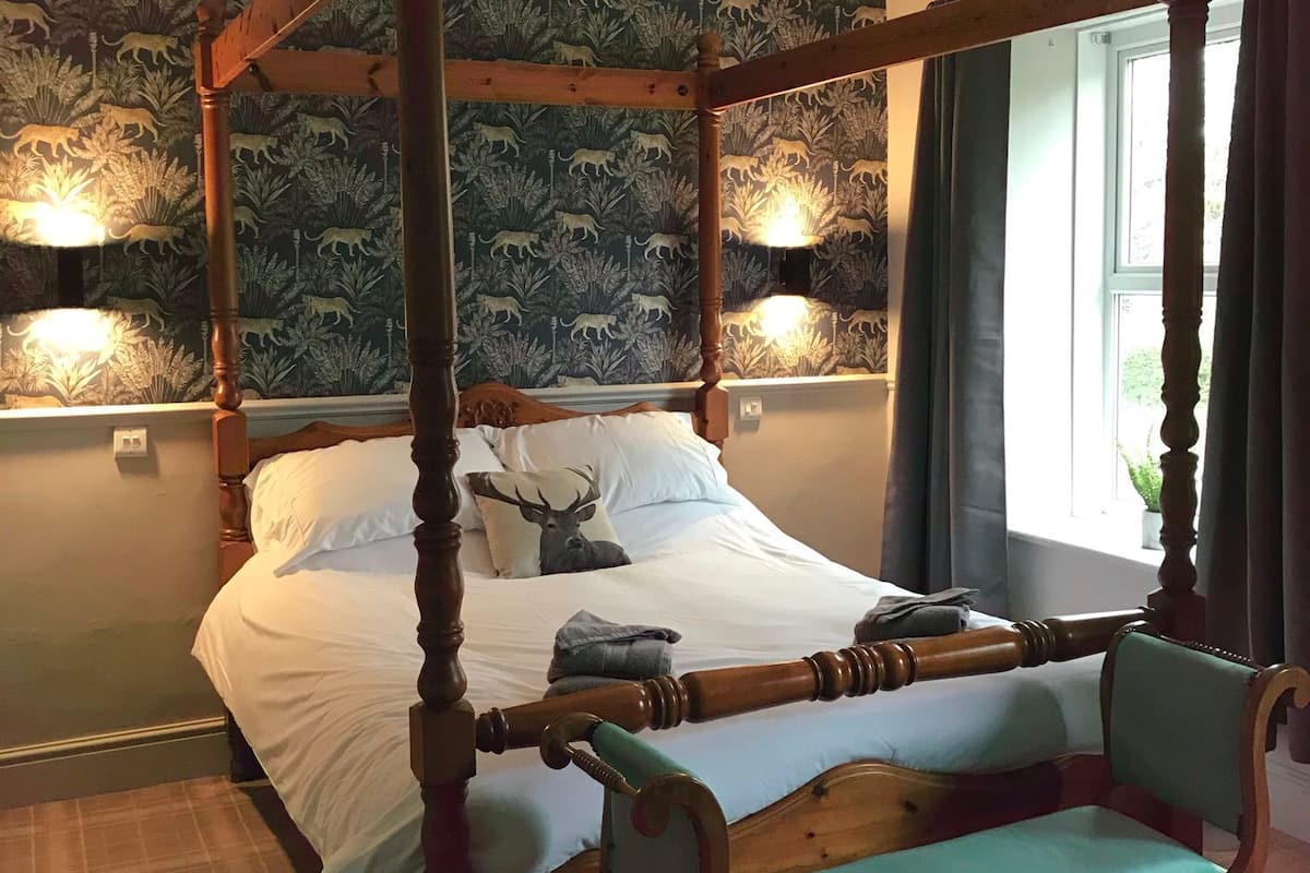 A four-poster bed with a canopy, a bench, and a wall-mounted light fixture.