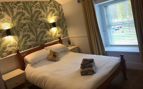 A neatly made bed with a pillow featuring a deer, a bedside lamp, and a window with blinds. - Red Lion Coaching Inn (Gainsborough)