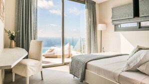 Una habitación de hotel moderna con una cama, un escritorio, una silla y un amplio ventanal con vistas al océano.