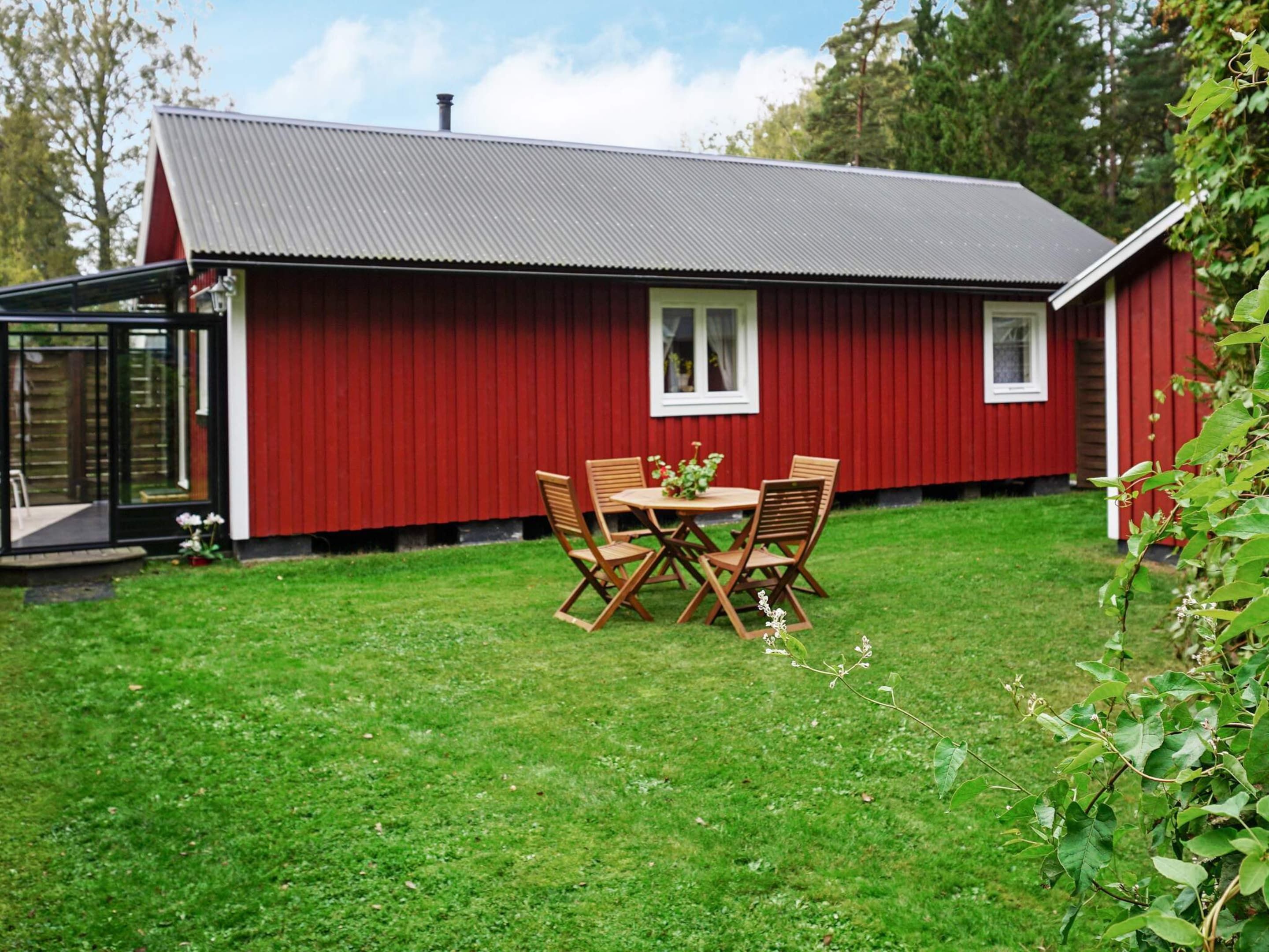A red wooden house with a metal roof, a glass door, and a small patio with a table and chairs.