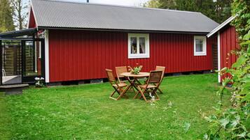 Un edificio rojo con techo de metal, puerta de cristal y un pequeño patio con sillas y mesa de madera.