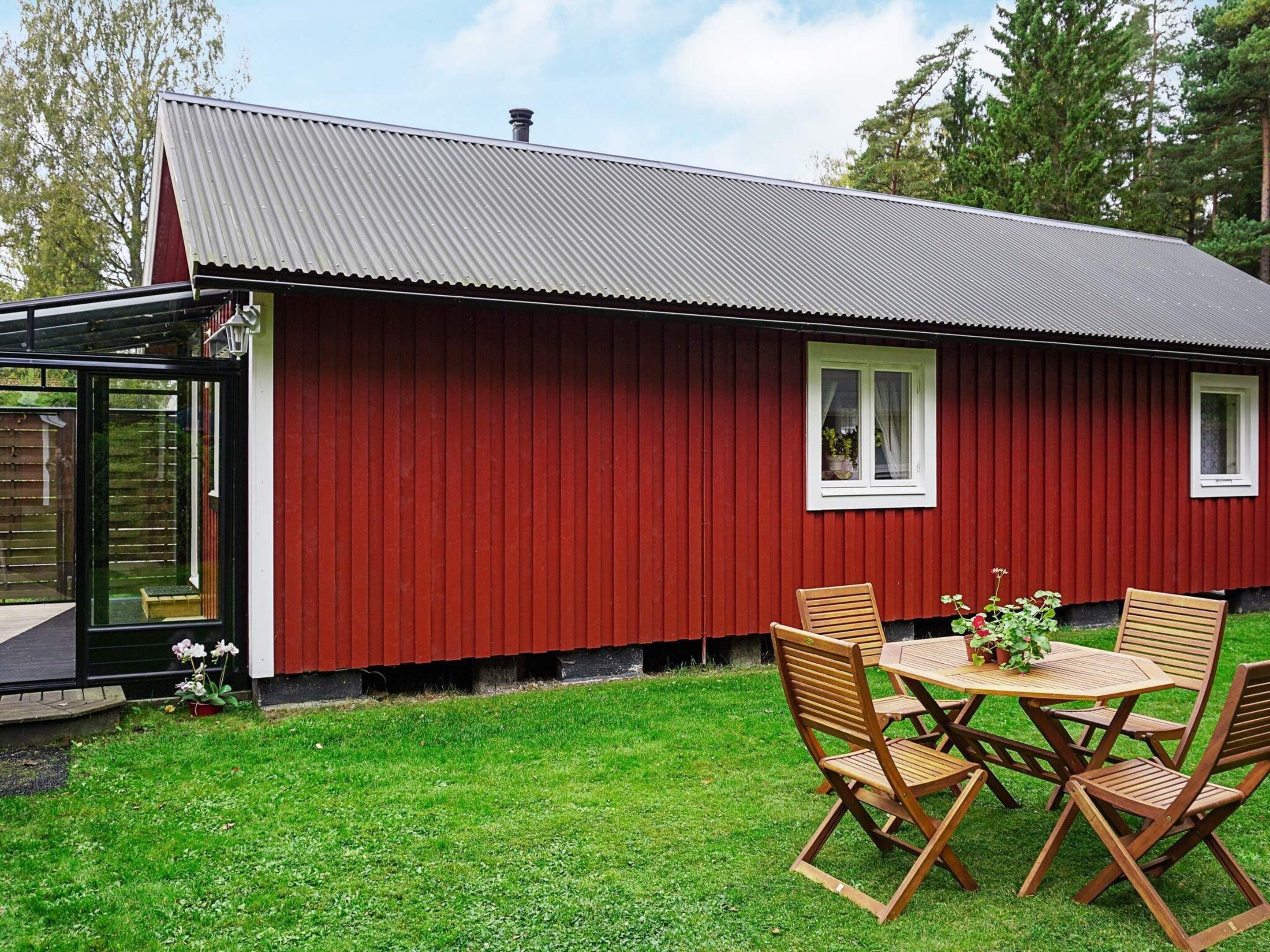 Un bâtiment rouge avec un toit en métal, une porte en verre et une petite terrasse dotée de chaises et d’une table en bois.