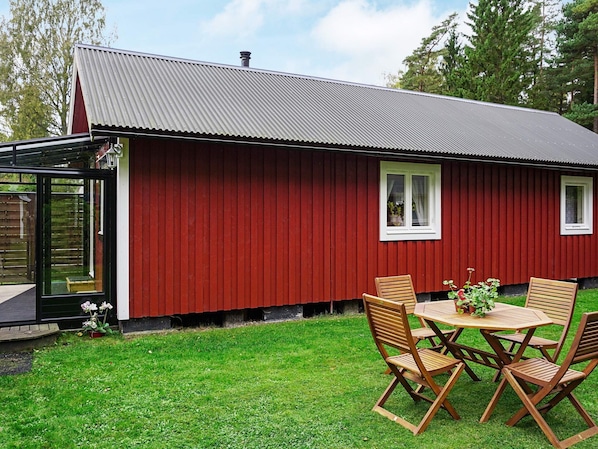 A red building with a metal roof, a glass door, and a small patio with wooden chairs and a table.