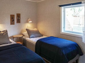 A room with two beds, a small table, a lamp, and a window. - 4 Person Holiday Home in Byxelkrok (Byxelkrok)
