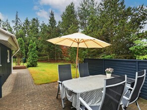 A patio with a table and chairs, an umbrella, and a garden with trees. - 4 Star Holiday Home in Hals (Hals)