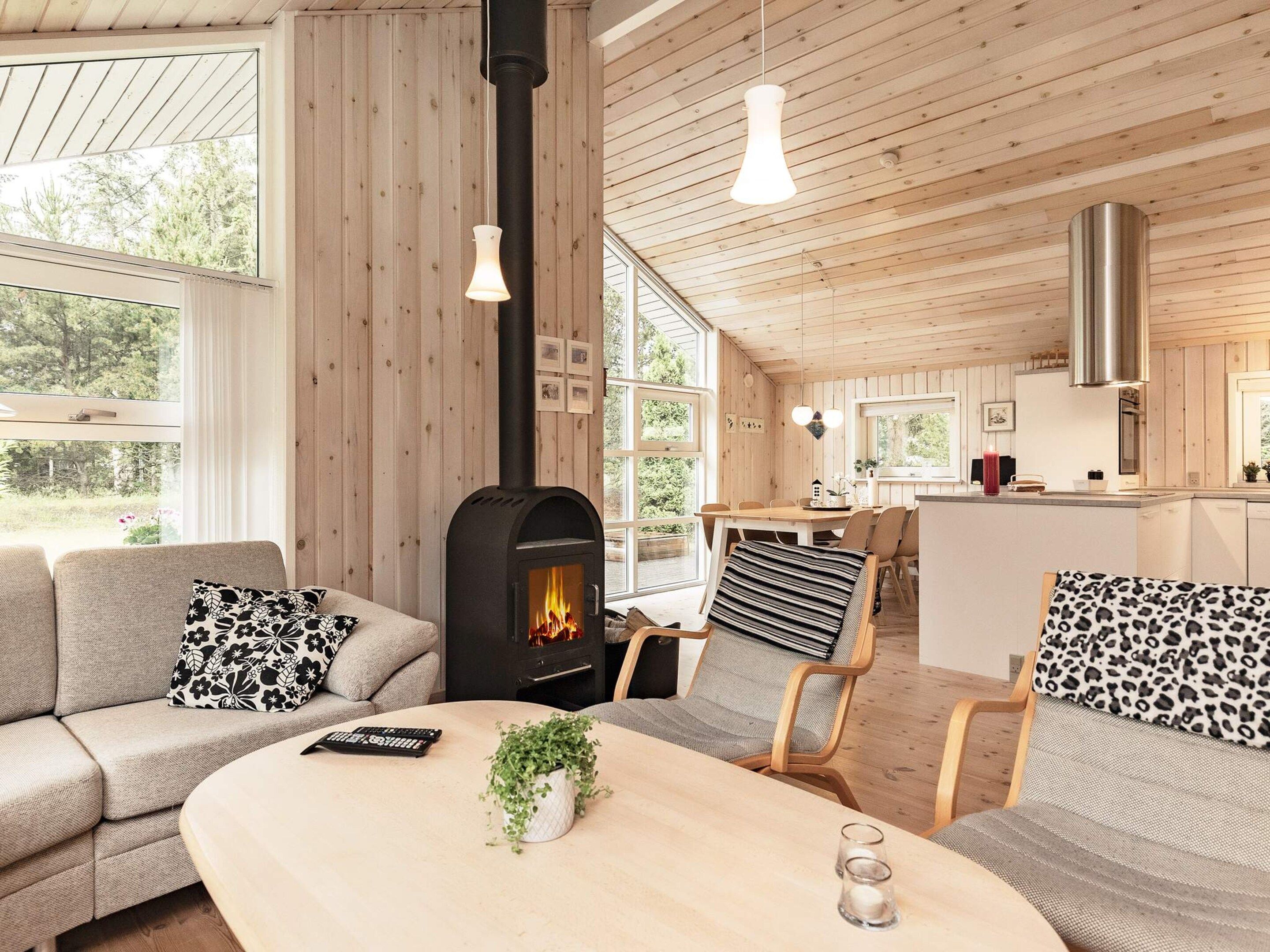 Ein gemütliches Wohnzimmer mit Kamin, Holzmöbeln und einem Essbereich, im Hintergrund ist eine Küche zu sehen.