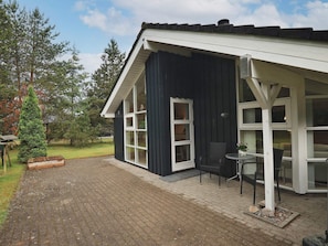 A building with a dark exterior, white trim, and a covered patio area with a table and chairs.