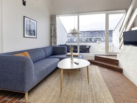 Una sala moderna con un sofá azul, una mesa de centro redonda y un amplio ventanal con vistas a un edificio.