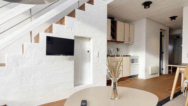 Un interior modern amb una escala, una zona de cuina i un espai menjador amb un comandament a la taula.