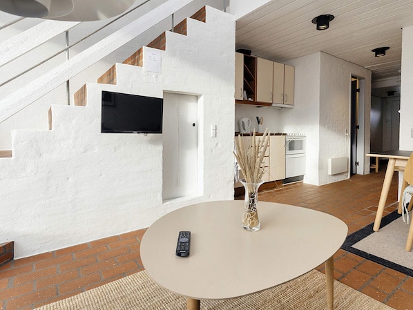 A modern interior with a staircase, a kitchen area, and a dining space with a remote control on a table.