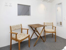 Una habitación con dos sillas de madera, una mesita, un ventanal y un espejo en la pared.