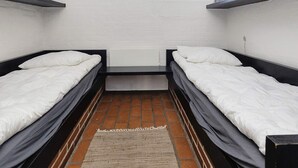Habitació amb dos llits, una finestra i un terra de maons.
