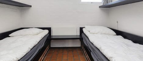 A room with two beds, a window, and a brick floor.