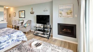 A living room with a fireplace, a TV, a sofa, and a patterned rug. - Cozy Ocean View Condo - Ground Floor - Fireplace! (Lincoln City)
