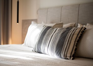 Una cama con una colcha blanca y almohadas a rayas.