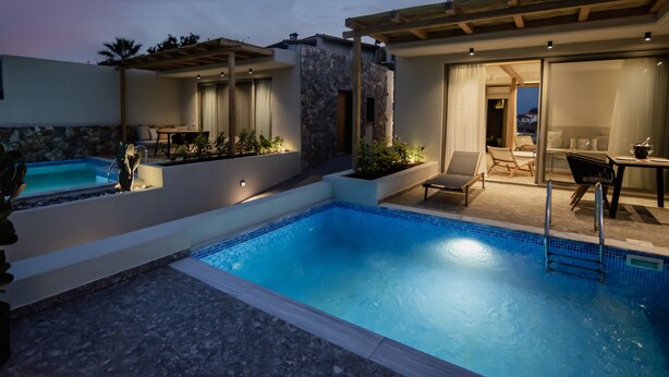 A pool area with a stone wall, lounge chairs, and a table with chairs. - Kaktus Suites Private Pool (Kassandra)