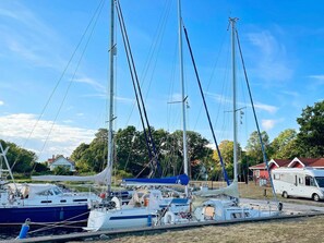A marina with multiple sailboats docked, a trailer, and a building in the background.