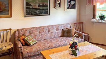 Una sala de estar con un sofá estampado, una mesa de centro de madera con un florero, un reloj y cuadros en la pared.