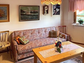 A living room with a patterned sofa, a wooden coffee table with a vase of flowers, a clock, and framed artwork on the wall.