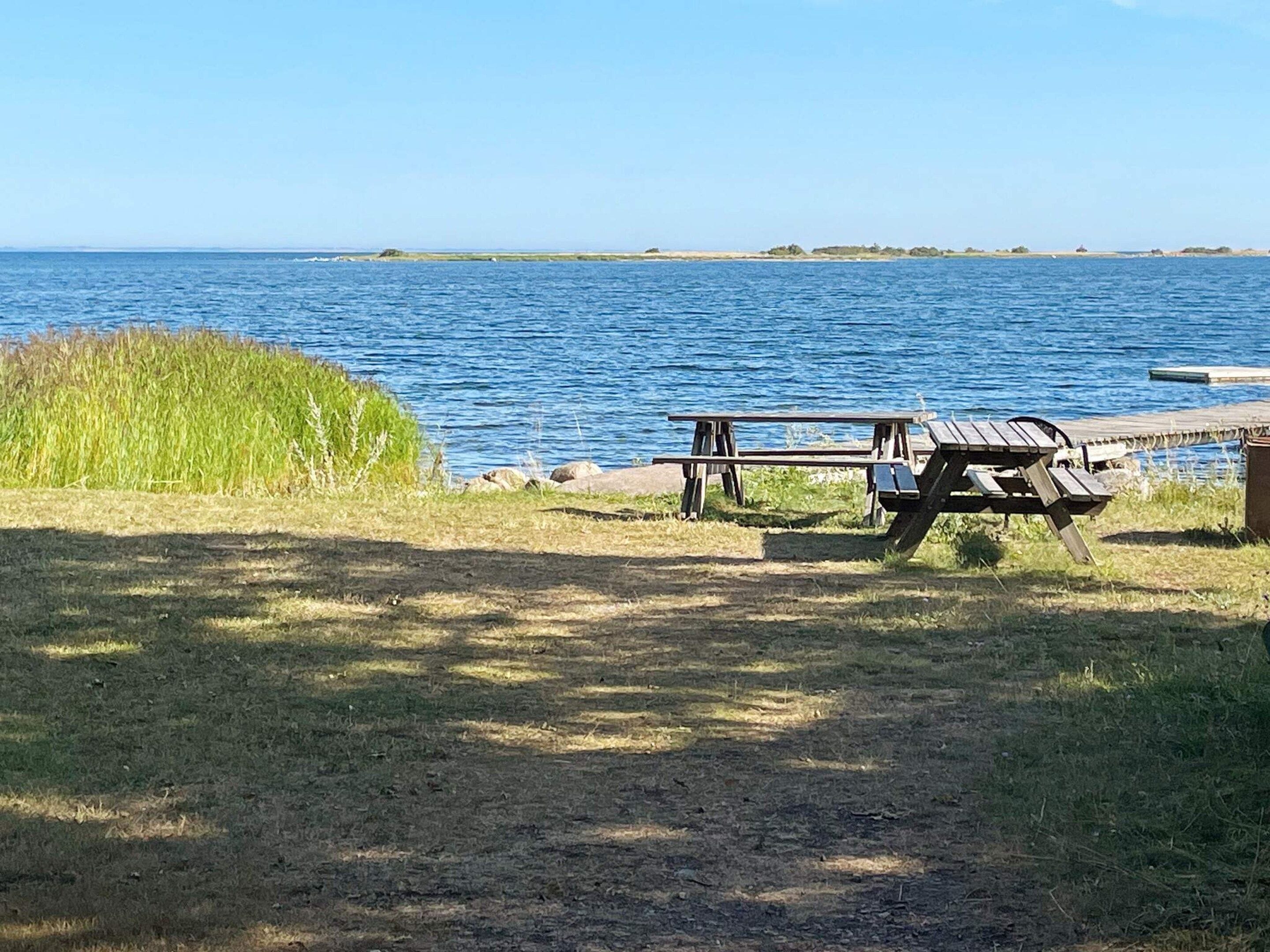 A picnic table by a lake with grassy areas and a clear sky.