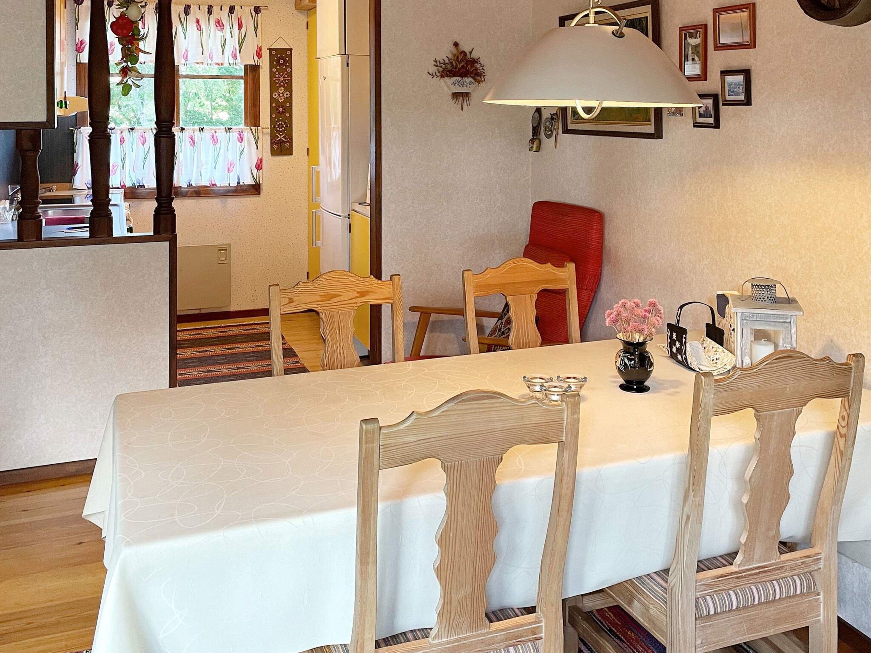 Un comedor con una mesa dispuesta para cuatro personas, sillas de madera, una lámpara y un florero con flores.
