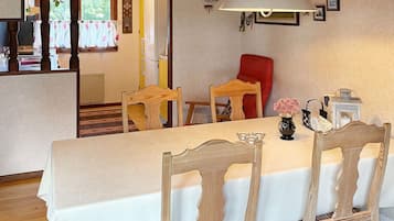Un comedor con una mesa dispuesta para cuatro personas, sillas de madera, una lámpara y un florero con flores.