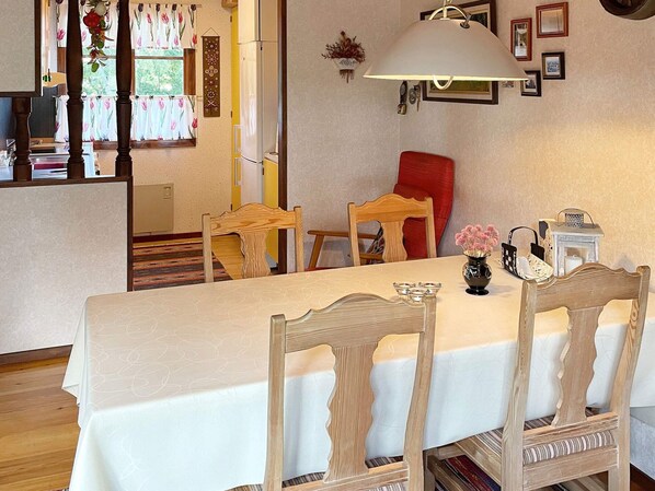 A dining area with a table set for four, wooden chairs, a lamp, and a vase with flowers.