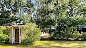 A small wooden structure with a door, surrounded by grass and trees. - 7 Person Holiday Home in Hagby (Ljungbyholm)