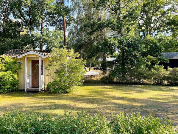 Une petite construction en bois, dotée d’une porte, entourée d’herbe et d’arbres.