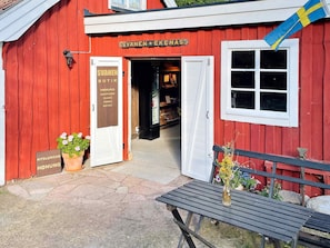 Un bâtiment rouge avec une enseigne indiquant « SVANEN EKENAS » et un drapeau suédois. On y voit un banc et un pot de fleurs devant l’entrée.
