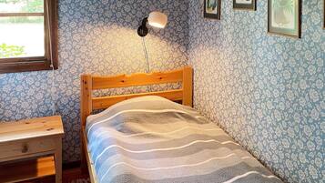A bedroom with a wooden bed, a bedside table, a lamp, and floral wallpaper.