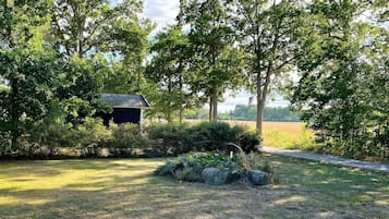 A rural landscape with a wooden structure surrounded by lush greenery and a clear sky.
