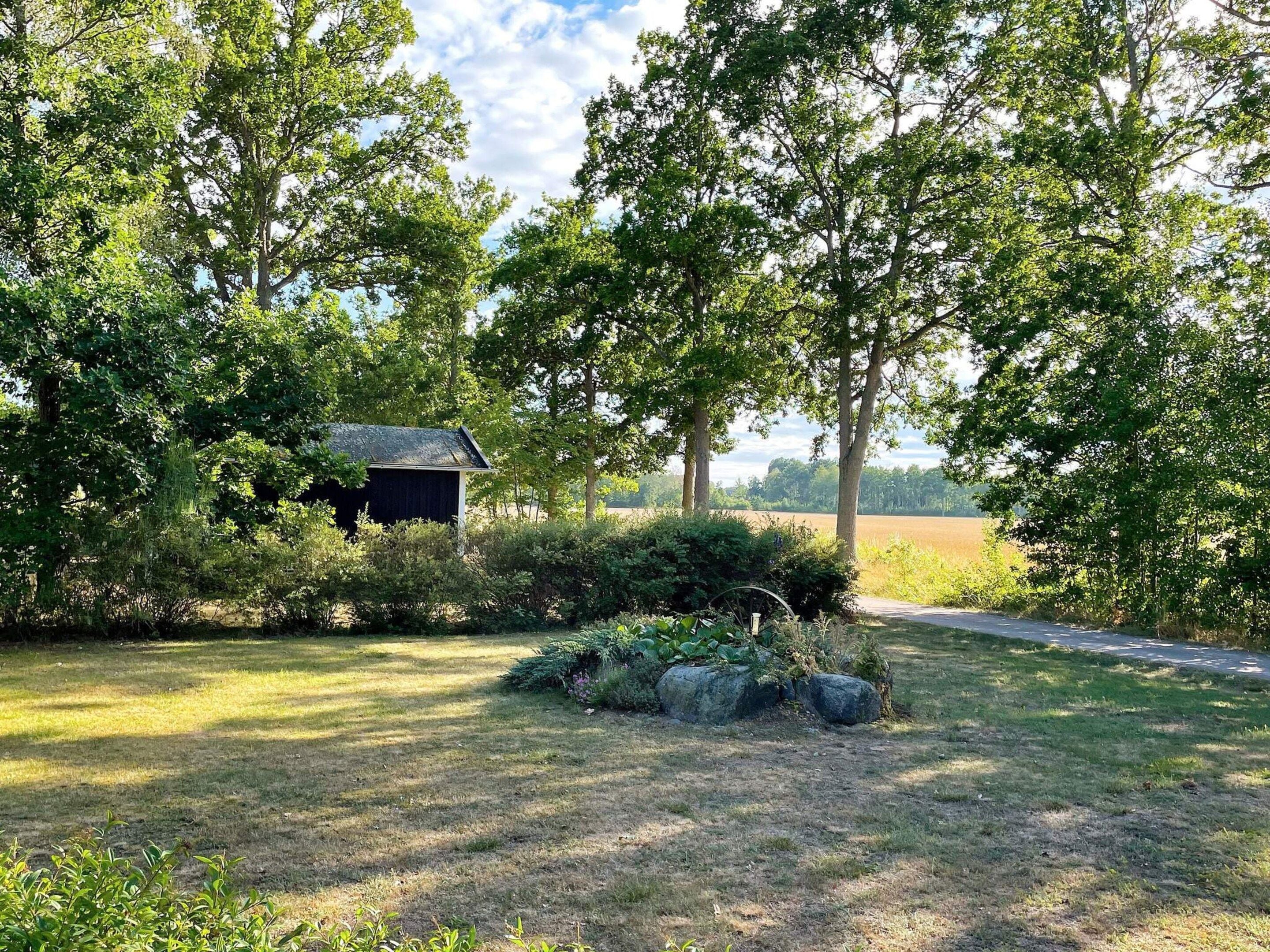 A rural landscape with a wooden structure surrounded by dense foliage and a clear sky.